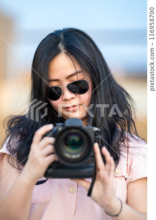 Amateur sunglasses Asian Woman take a photo with professional mirrorless camera at outdoor blue rooftop building in twilight time. 116958700