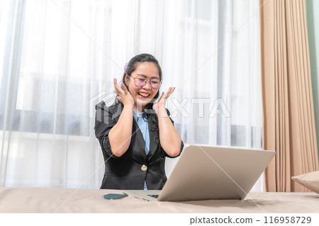 The woman was excited to look at a laptop which was laid on her bed because of her winning a lottery. She wearing glasses was screaming in her transparent curtain bedroom. 116958729