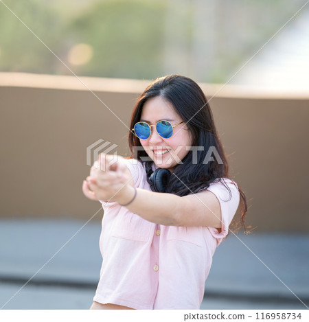 Asian woman in the pink shirt is playing finger gun, aim and focus on it. She relaxes and smiles between acting. The environment around building rooftop in Twilight time. Asian woman in the pink shirt is playing finger gun, aim and focus on it. She relaxes and smiles between acting. The environment around building rooftop in Twilight time. 116958734