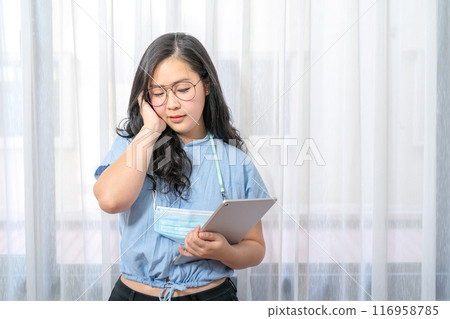 Concentrated Asian Glasses Woman focus looks at her tablet in hand in private room in work at home periodically. PathumThani Thailand. Concentrated Asian Glasses Woman focus looks at her tablet in hand in private room in work at home periodically. PathumThani Thailand. 116958785
