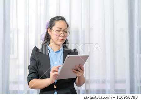 Concentrated Asian Glasses Woman focus looks at her tablet in hand in private room in work at home periodically. PathumThani Thailand. Concentrated Asian Glasses Woman focus looks at her tablet in hand in private room in work at home periodically. PathumThani Thailand. 116958788