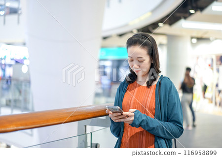 Beautiful Asian Woman holds and plays mobile phone in Department Store atmosphere environment in Bangkok City. 116958899