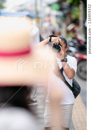 Professional Asian Camera man focus on the image with his mirrorless camera beside the street outdoor field. Professional Asian Camera man focus on the image with his mirrorless camera beside the street outdoor field. 116959332