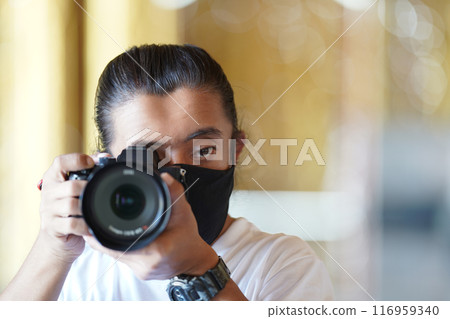 A man wearing black mask is shooting photo through a viewfinder camera with the right eye. A man wearing black mask is shooting photo through a viewfinder camera with the right eye. 116959340