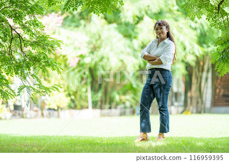 Pretty woman wearing a trusty white jeans shirt and pretty smile to the camera under the tree outside field. Pretty woman wearing a trusty white jeans shirt and pretty smile to the camera under the tree outside field. 116959395