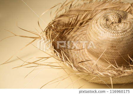 A large summer straw hat from which protruding straws on a sand-colored background 116960175