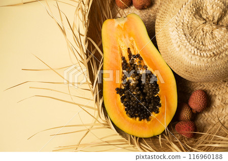 Half of juicy ripe papaya and lychee berry lying on straw hat on yellow background, top view 116960188