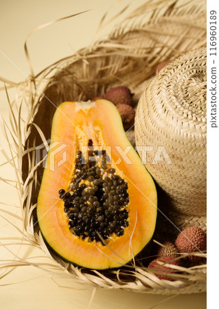 Half of juicy ripe papaya and lychee berry lying on straw hat on yellow background, top view Half of juicy ripe papaya and lychee berry lying on straw hat on yellow background, top view 116960189