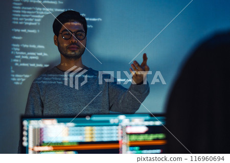 Indian man programmer standing in front of a screen with code projected presentation the integration of technology and human expertise in software development Indian man programmer standing in front of a screen with code projected presentation the integration of technology and human expertise in software development 116960694
