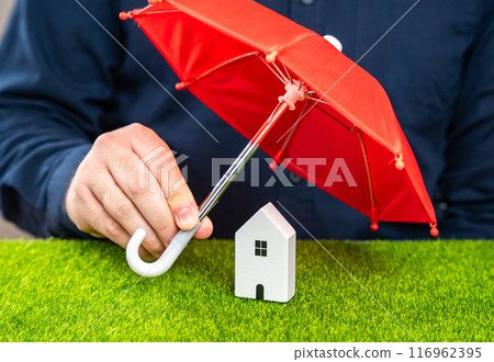Man covering house with red umbrella. Insurance concept. Be prepared for unforeseen events. Repairs or rebuilding in the event of a covered loss. Man covering house with red umbrella. Insurance concept. Be prepared for unforeseen events. Repairs or rebuilding in the event of a covered loss. 116962395