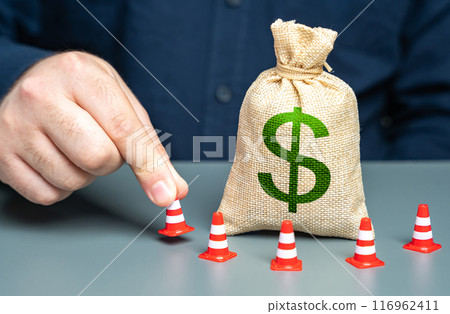 A man surrounds a dollar money bag with cones. Financial restrictions and sanctions. Freezing of capital, seizure of funds. Limitation on use of dollar transactions. Regulatory budget spending policy 116962411