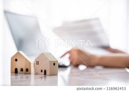 Close up wooden house model with hand using laptop for financial analysis for real estate 116962453