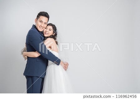 Happy smiling Asian couple in love in wedding dress embracing each other on white background Happy smiling Asian couple in love in wedding dress embracing each other on white background 116962456