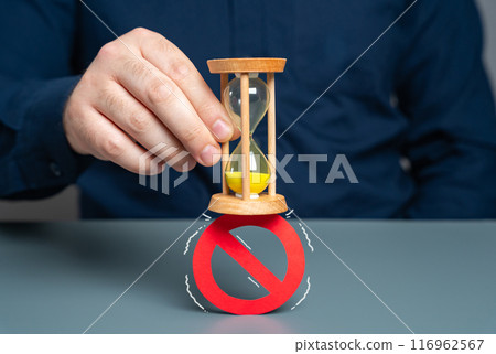A man crushes a prohibition sign with an hourglass. Concept of lifting prohibitions and restrictions due to expiration of time, irrelevance. Review laws, regulations. Liberalization and legalization. 116962567