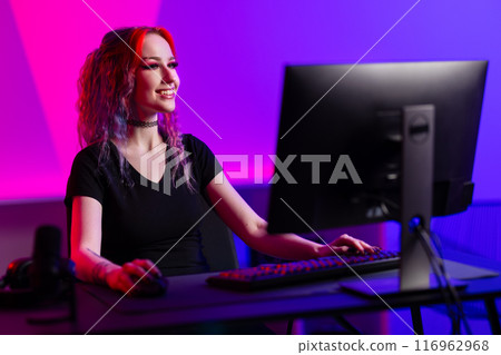 Professional gamer smiling while playing a PC game in a vibrant room with neon lighting 116962968