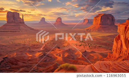 A vast desert with towering red rocks basks in a sunsets golden hues, creating a warm, ethereal glow. 116963055