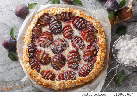 Open fruit plum pie galette with almonds close-up on wooden board. Horizontal top view 116963694