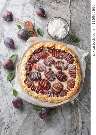 Autumn Sweet plum pie galette with almonds close-up on wooden board on table. Vertical top view 116963696