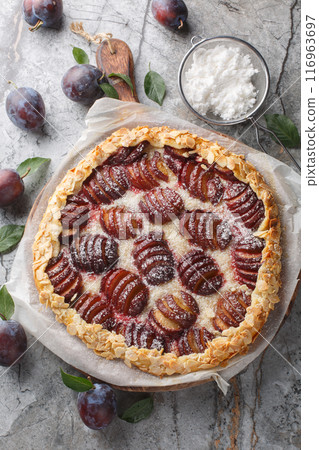 Summer plum galette with almonds and powdered sugar close-up on wooden board. Vertical top view 116963697
