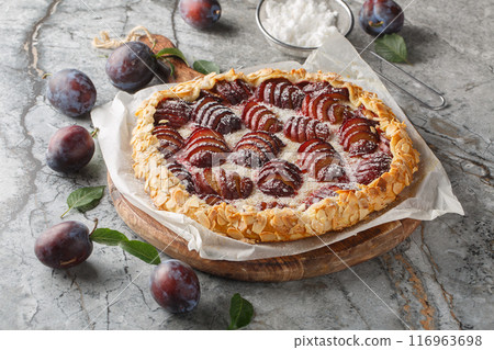 Open fruit plum pie galette with almonds close-up on wooden board. Horizontal 116963698