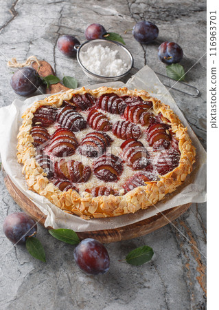 Summer plum galette with almonds and powdered sugar close-up on wooden board. Vertical Summer plum galette with almonds and powdered sugar close-up on wooden board. Vertical 116963701