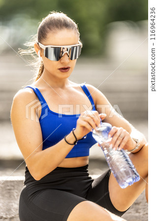 Young sporty woman drinking water from a bottle after exercising at the park 116964236