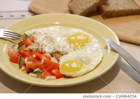 Fried eggs with tomatoes and cucumbers on a plate with bread.  116964254