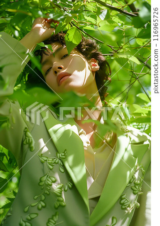 A woman is wearing a green jacket and is posing in a forest A woman is wearing a green jacket and is posing in a forest 116965726