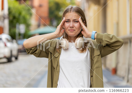 Displeased exhausted young Caucasian woman girl rubbing temples to cure headache on city street 116966223