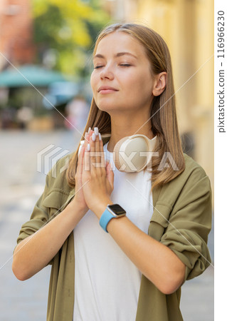 Young Caucasian woman meditating, breathes deeply with hands clasped, praying eyes closed on street 116966230