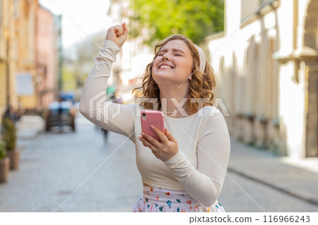 Young woman use mobile smartphone celebrating win good message news outdoors in urban city street Young woman use mobile smartphone celebrating win good message news outdoors in urban city street 116966243