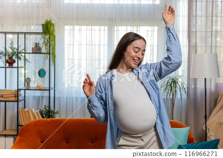 Happy smiling young pregnant woman playfully dancing listening music with big belly at home Happy smiling young pregnant woman playfully dancing listening music with big belly at home 116966271