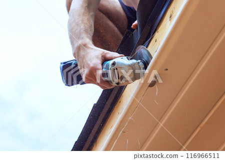 In employee is cutting off existing vinyl soffit plastic panels to specific size on facade ceiling of new house 116966511
