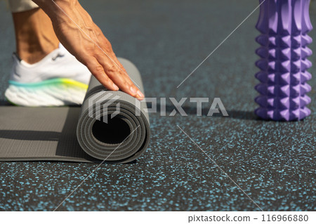 Man hands unrolling yoga mat before practice at sports ground. Outdoor. Copy space. Yoga, sport, healthy lifestyle concept. Close up. 116966880