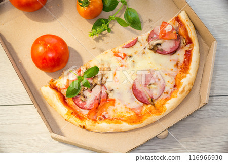 cooked pizza with salami and sausage in a box on a wooden table 116966930