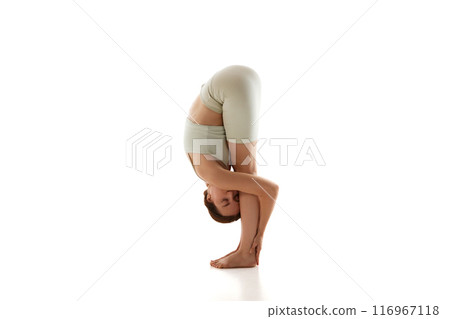Sporty woman posing in forward bend, enhancing flexibility and releasing tension, shows benefits of regular yoga practice against white background. 116967118