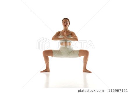 Focused and balanced, woman engages in yoga routine that enhances her strength and flexibility against white studio background. 116967131