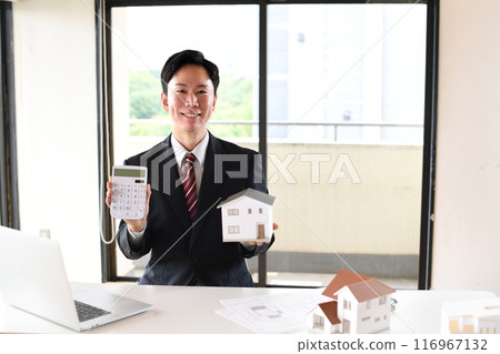 Young Asian man in a suit holding a house model and a calculator 116967132