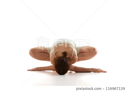 During yoga session, fit young woman performs deep forward fold, enhancing her flexibility against white studio background. 116967139