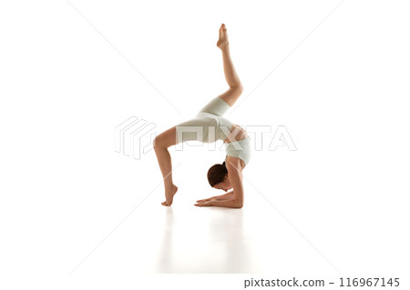 Athletic woman demonstrates one-legged forearm wheel pose against white studio background. Advanced yoga training 116967145