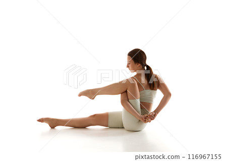 Fit woman practices seated leg twist, focusing on flexibility and spinal alignment, important aspects of her comprehensive yoga training. 116967155