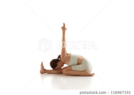 Athletic woman performs seated forward bend with twist, enhancing flexibility and spinal stretching, during yoga session against white background. 116967191