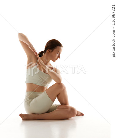 Woman practices seated twist, focusing on spinal flexibility and detoxification against white studio background, promoting relaxation. 116967221