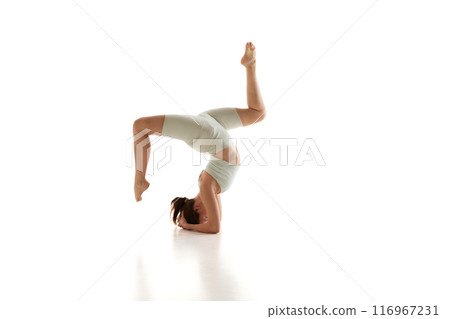 Practicing headstand, athletic woman focuses on building strength and mental resilience against white studio background. Yoga. 116967231