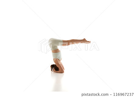 Woman practices headstand, building core strength against white studio background. Training and enhancing overall body control and awareness. 116967237