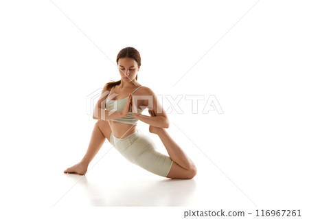 Woman in athletic wear performs yoga pose, stretching her leg, standing on knee and holding hands in Namaste against white studio background. 116967261