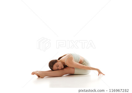 Athletic woman in fitness wear performs seated forward bend yoga pose against white studio background. Calmness. 116967282