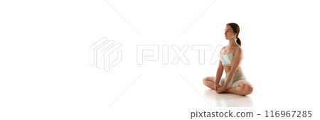Banner. Young woman sitting in lotus-yoga pose, crossed legs against white studio background with negative space to insert text. 116967285