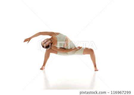 Woman in athletic wear performs wide-legged yoga pose, stretching her back and arms against white studio background. Control and balance. 116967299