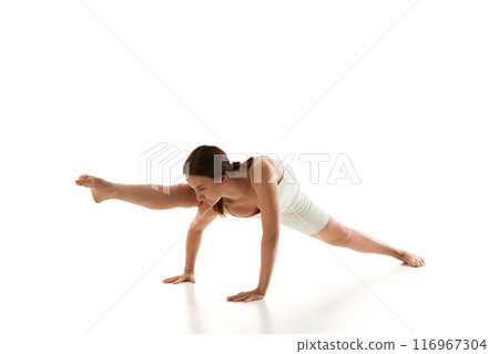 Woman in athletic wear performs challenging yoga pose showcasing strength and balance against white studio background. 116967304